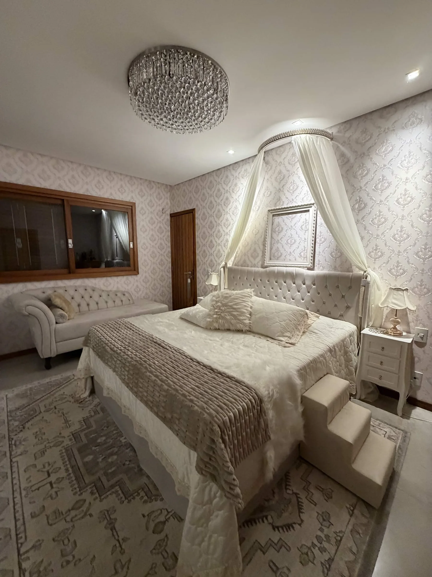Depois — Quarto transformado em tons claros, com capitonê, dossel, papel de parede e lustre de cristal